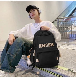Detailed view of black nylon backpack with large KMGDM lettering and white plush doll charm