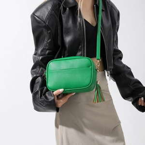 Détail d'un sac bandoulière vert en similicuir avec pompon élégant et finitions métalliques dorées
