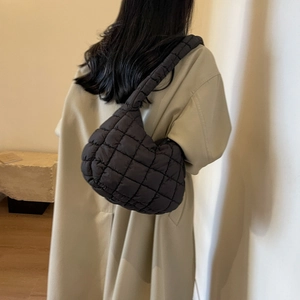 Détail d'un sac à bandoulière matelassé noir porté avec un trench-coat beige chic