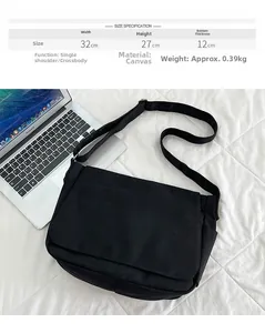 Détail du sac bandoulière en toile noire minimaliste avec dimensions 32x27x12cm près d'un PC