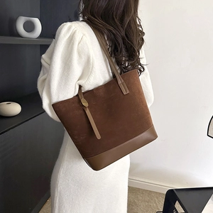 Détail d'un sac cabas en daim marron foncé porté avec une robe en maille blanche chic