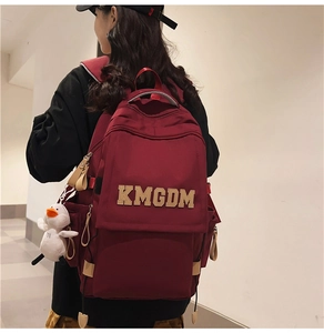 Detail of burgundy nylon backpack featuring letter patch and a cute white duck pendant charm
