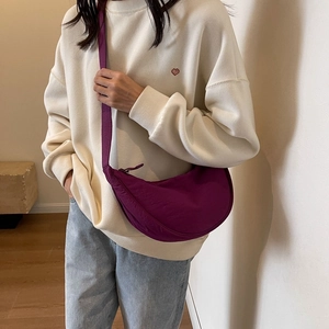 Close-up of a purple crescent-shaped nylon crossbody bag worn by a model in casual style