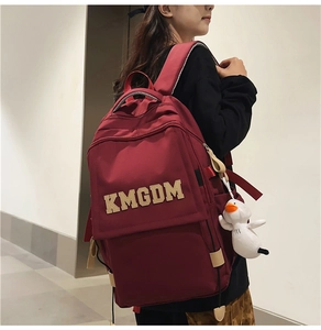 Detail of burgundy nylon backpack with KMGDM patch and a cute white duck pendant