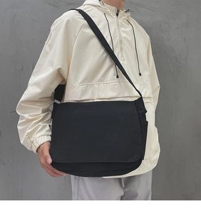 Détail d'un grand sac bandoulière noir en toile porté par un mannequin en style streetwear