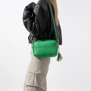 Sac bandoulière vert en cuir avec pompon porté par un mannequin en veste noire