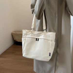 Detail of cream canvas tote bag with side pockets and fashion label on windbreaker