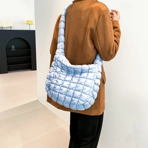 Close-up of light blue quilted crossbody bag with soft padded nylon texture on model