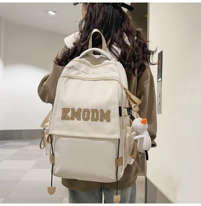 Close-up of cream nylon backpack featuring varsity KMGDM patch and plush duck charm