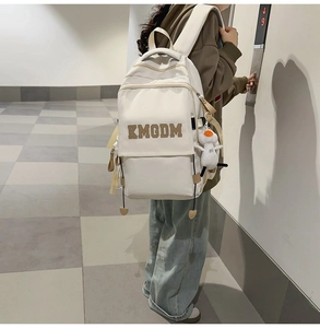 Detail shot of white nylon backpack with KMGDM embroidery and plush duck charm