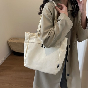 Detail view of the side pocket and black FASHION label on this cream canvas tote bag