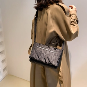 Dettaglio della borsa a tracolla trapuntata nera con zip argento su cappotto camel