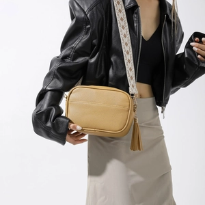 Détail d'un sac bandoulière jaune en PU avec large sangle géométrique et pompon en cuir