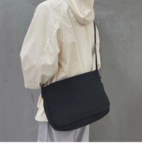 Sac messager minimaliste en toile noire porté à l'épaule sur fond industriel