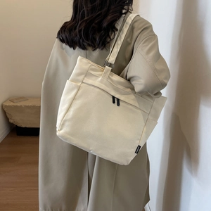 Minimalist cream canvas tote bag with side fashion label shown on model's shoulder