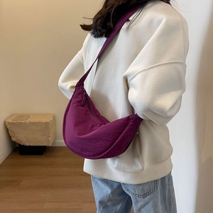 Detail of purple crescent shoulder bag showing nylon texture and draped shape on a model