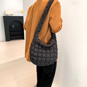 Side view of a black quilted puffer shoulder bag with square padding texture on a model