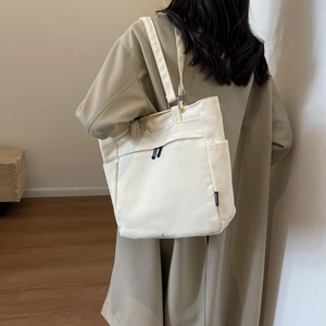 Close-up of cream canvas tote bag with functional pockets worn with beige trench coat
