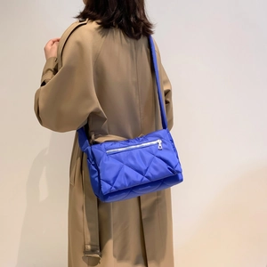 Dettaglio della borsa a tracolla in nylon trapuntato blu reale indossata su un trench kaki