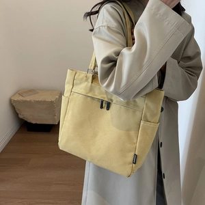 Detail of yellow canvas tote bag featuring a front zipper pocket and fashion tag