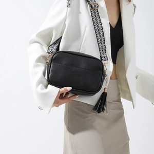 Détail du sac bandoulière noir en similicuir avec large sangle géométrique et pompon