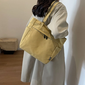 Detail of yellow canvas tote bag with front zipper pocket and fashion patch on side