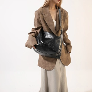 Detail view of glossy black PU leather hobo bag with gold hardware on a model