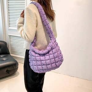 Detailed side view of a purple quilted nylon cloud bag worn by a model in a minimalist room