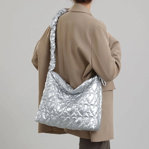 Detail of silver metallic quilted tote bag with heart patterns and ruffled strap on model