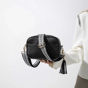 Détail du sac à bandoulière en cuir noir avec large sangle géométrique et pompon