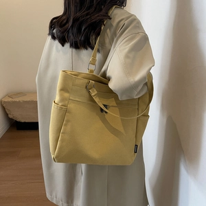 Detail of a mustard yellow canvas tote bag featuring a stitched fashion side label tag