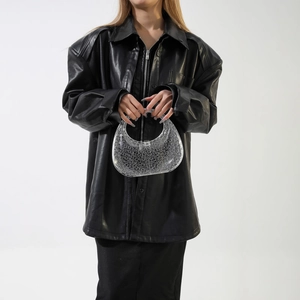 Detail of transparent PVC crescent handbag with circular texture and black leather jacket