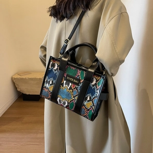 Detail of colorful snake-print tote bag with black strap worn by model in beige coat