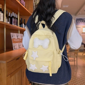 Detail of yellow nylon backpack featuring white star patches and plush bow decoration
