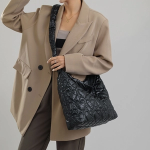 Detail shot of black heart-quilted nylon puffer tote bag carried by a model