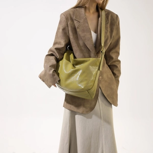 Detailed view of avocado green leather bag texture on model with brown suit