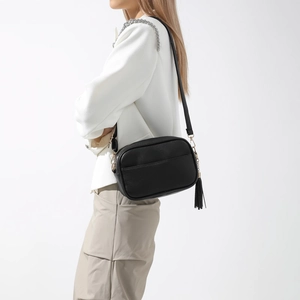 Détail du sac caméra noir grainé avec pompon et garnitures dorées porté par le modèle