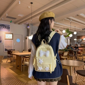 Pale yellow nylon backpack featuring plush star decor worn in a cozy cafe setting