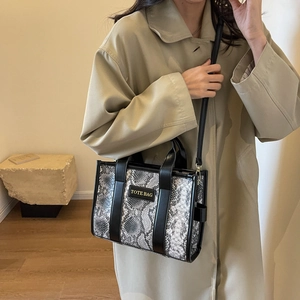 Detailed view of snake-print tote bag with gold lettering on a stylish trench coat