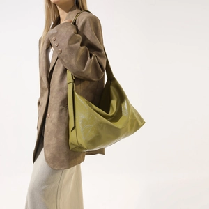 Olive green faux leather tote bag with glossy texture and soft folds on model