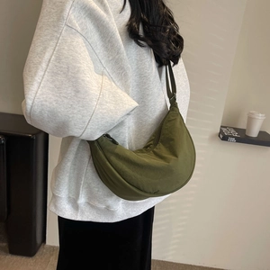Detail view of a dark green nylon crescent bag worn crossbody with adjustable strap