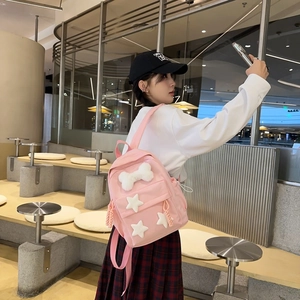 Pink nylon backpack featuring white plush bone decor and star patches in a lifestyle view