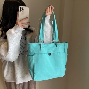 Detail of mint green canvas tote bag showing side pocket and fashion label tag