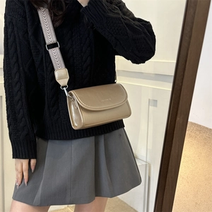 Detail of champagne gold crossbody bag with decorative wide woven shoulder strap on model