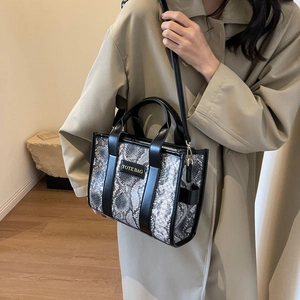 Detail view of the gray snake-print tote bag featuring black leather trim and long strap