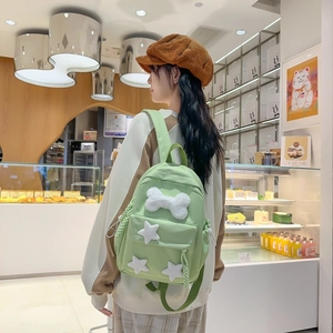 Detail view of a light green nylon backpack with white plush bone and star decorations