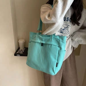 Minimalist mint green canvas tote bag with side pocket shown on shoulder by model