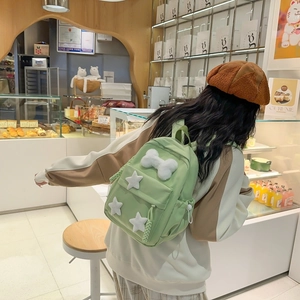 Detail of light green nylon backpack with plush star and bone charms in a cozy cafe setting