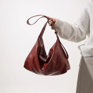Detail of burgundy hobo bag in glossy leather with gold buckle worn with white sweater