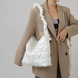 Detail of white heart-quilted shoulder bag with ruched cloud-style strap on model